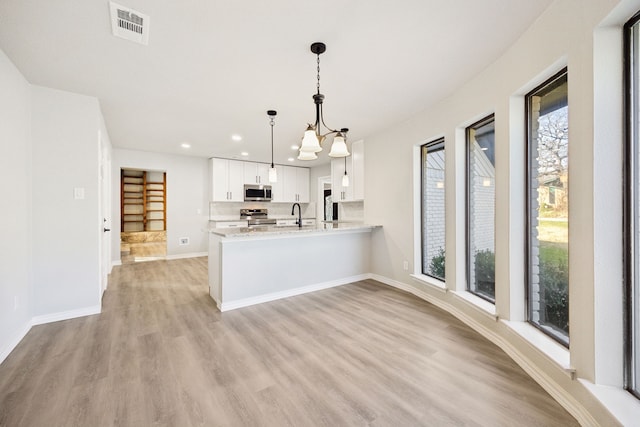 kitchen with appliances with stainless steel finishes, decorative light fixtures, white cabinetry, kitchen peninsula, and light stone countertops