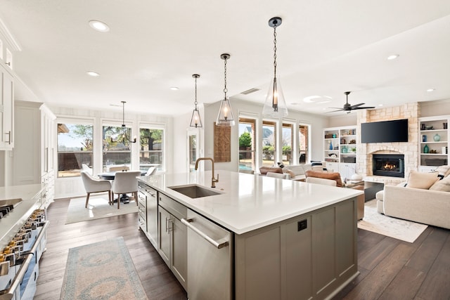 kitchen with dark wood-type flooring, sink, decorative light fixtures, appliances with stainless steel finishes, and an island with sink