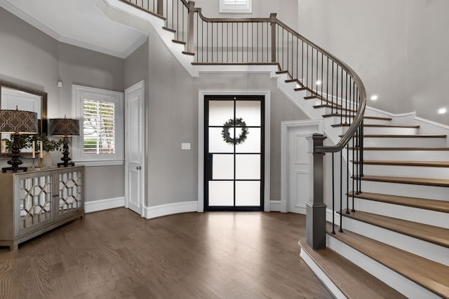 foyer entrance with a towering ceiling, wood-type flooring, and ornamental molding