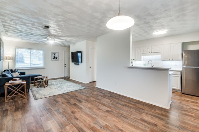 kitchen featuring pendant lighting, stainless steel refrigerator, sink, white cabinets, and dark wood-type flooring