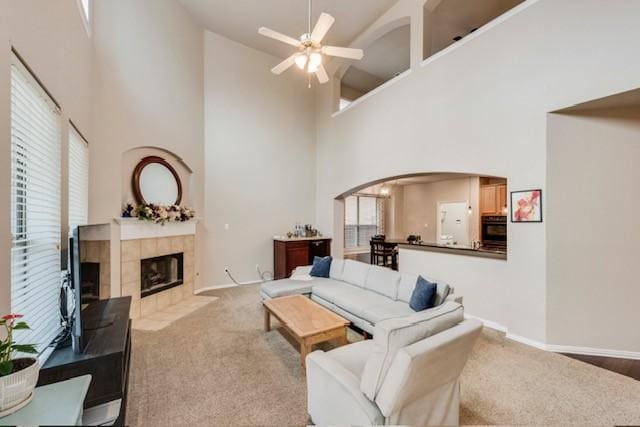 carpeted living room featuring plenty of natural light, a tile fireplace, ceiling fan, and a high ceiling