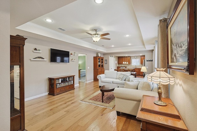 living room featuring crown molding, light hardwood / wood-style flooring, a raised ceiling, and ceiling fan