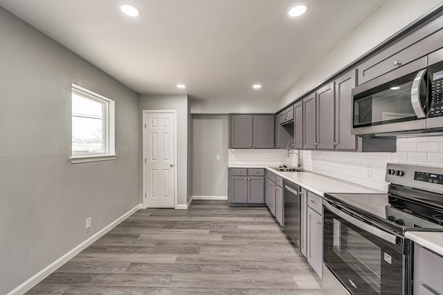 kitchen featuring sink, light hardwood / wood-style flooring, gray cabinets, appliances with stainless steel finishes, and decorative backsplash