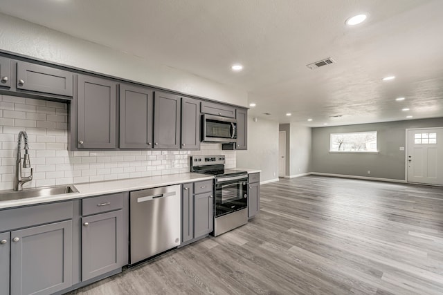 kitchen featuring sink, gray cabinetry, tasteful backsplash, appliances with stainless steel finishes, and light hardwood / wood-style floors