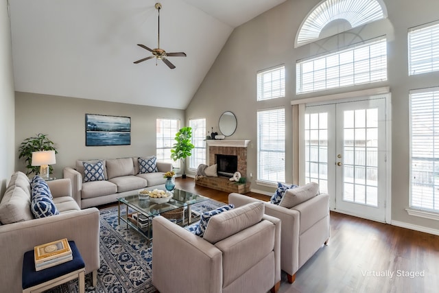 living room featuring high vaulted ceiling, wood-type flooring, ceiling fan, a brick fireplace, and french doors