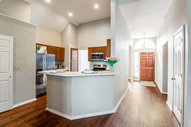 kitchen featuring appliances with stainless steel finishes, hanging light fixtures, a high ceiling, kitchen peninsula, and dark wood-type flooring