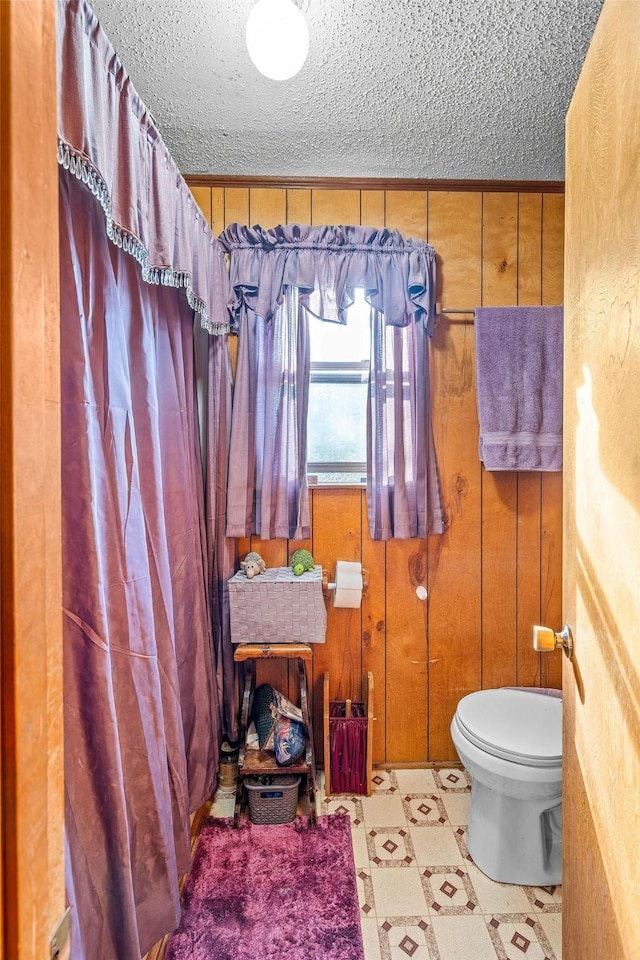 bathroom featuring a textured ceiling, toilet, and wood walls