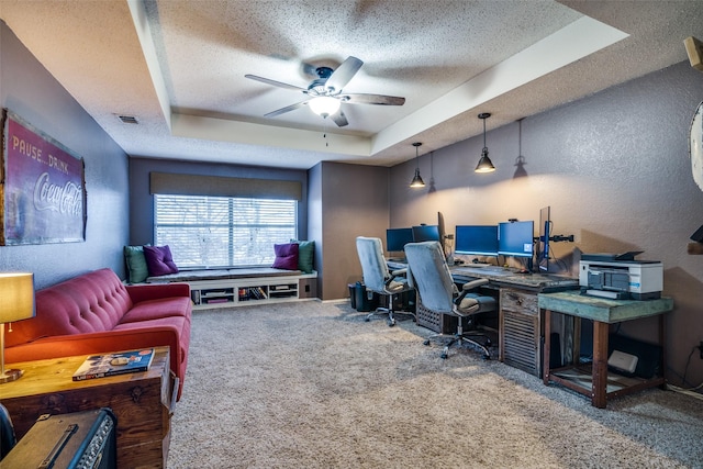 carpeted office space with ceiling fan, a textured ceiling, and a tray ceiling