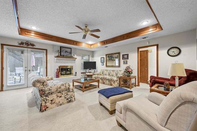 living area featuring a raised ceiling, light colored carpet, a fireplace, and french doors