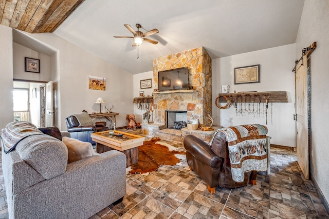 living room featuring a stone fireplace, vaulted ceiling, a barn door, and ceiling fan