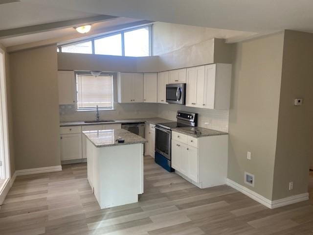 kitchen with sink, appliances with stainless steel finishes, white cabinetry, a center island, and lofted ceiling with beams