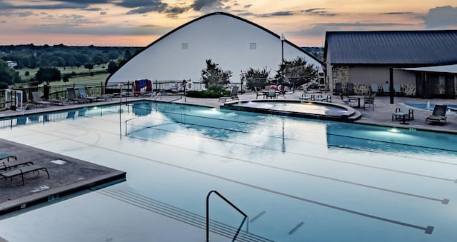 pool at dusk with a community hot tub and a patio