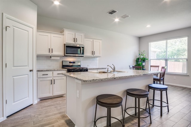 kitchen featuring sink, tasteful backsplash, a center island with sink, stainless steel appliances, and white cabinets