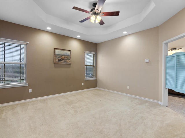 unfurnished room with a healthy amount of sunlight, light carpet, ceiling fan, and a tray ceiling