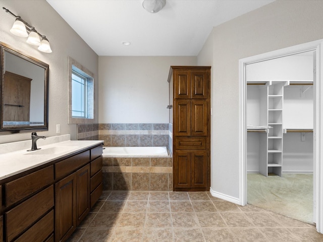 bathroom featuring a relaxing tiled tub, vanity, and tile patterned flooring