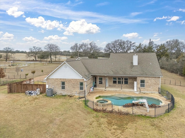 rear view of property with central AC, a swimming pool with hot tub, a patio, and a lawn