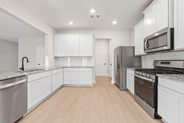 kitchen featuring stainless steel appliances, light stone countertops, white cabinets, and light hardwood / wood-style flooring