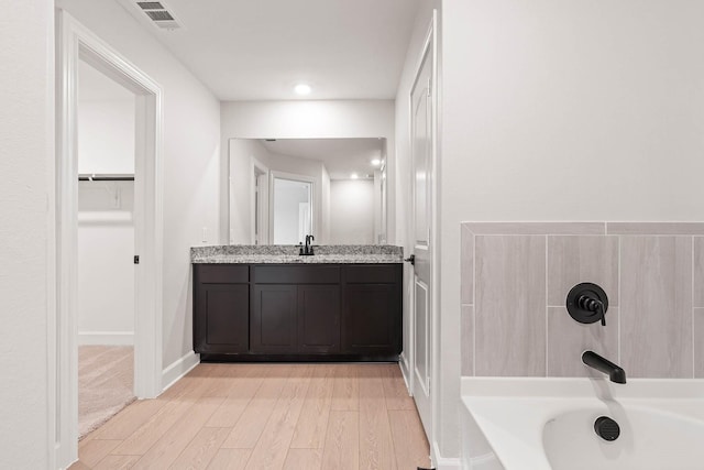 bathroom with hardwood / wood-style flooring, vanity, and a tub