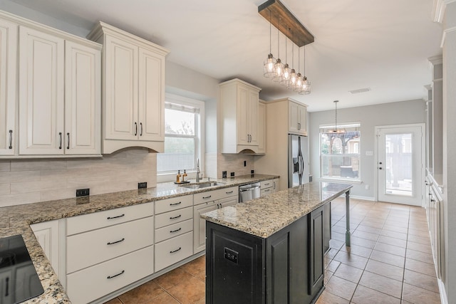 kitchen with sink, decorative light fixtures, a center island, appliances with stainless steel finishes, and light stone countertops