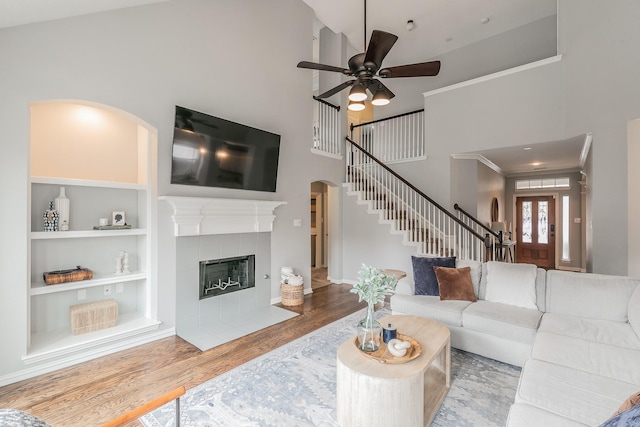 living room with built in shelves, hardwood / wood-style flooring, ceiling fan, a fireplace, and a high ceiling