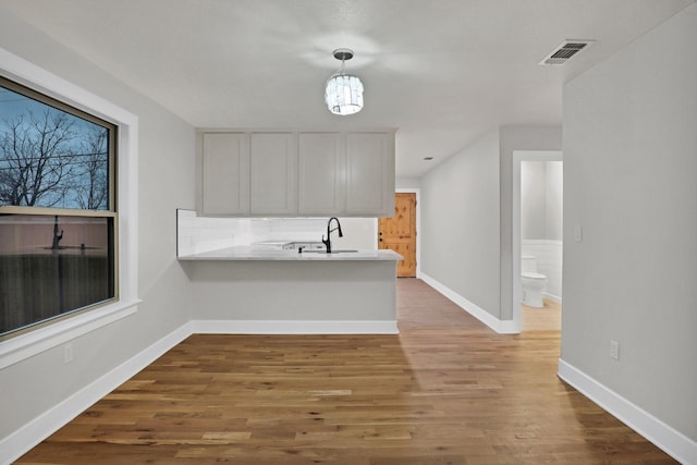 kitchen with hardwood / wood-style flooring, kitchen peninsula, hanging light fixtures, and white cabinets