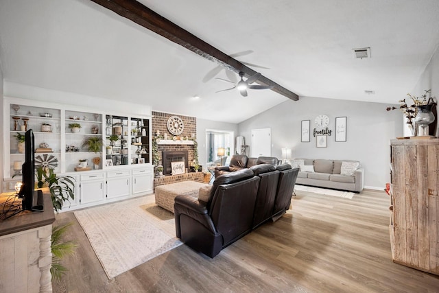 living room featuring a brick fireplace, lofted ceiling with beams, light hardwood / wood-style floors, and ceiling fan