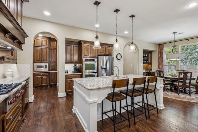 kitchen featuring an island with sink, dark wood-style floors, a kitchen bar, and appliances with stainless steel finishes