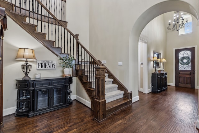 entrance foyer with arched walkways, wood finished floors, a towering ceiling, baseboards, and stairs