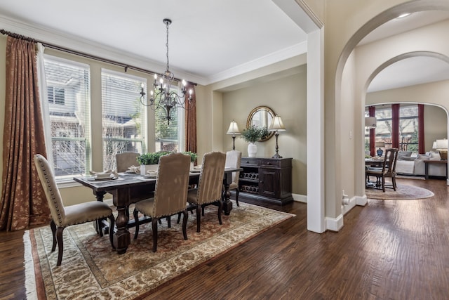 dining area featuring dark wood-style floors, arched walkways, ornamental molding, and baseboards