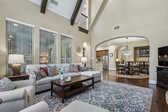 living room featuring dark wood-style floors, visible vents, arched walkways, and beamed ceiling