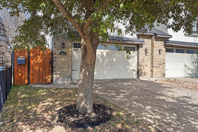 view of front of house with stone siding, concrete driveway, fence, and a gate