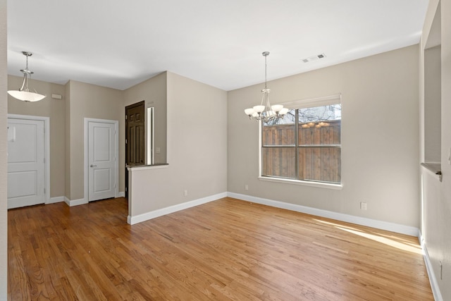 empty room featuring a notable chandelier, light wood-style flooring, visible vents, and baseboards