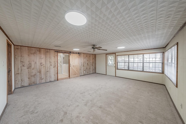 carpeted empty room featuring ceiling fan, a barn door, and wood walls