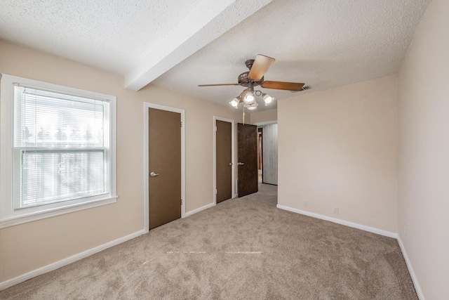 unfurnished bedroom featuring beam ceiling, light carpet, and a textured ceiling