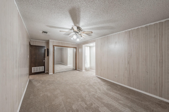 spare room featuring wood walls, a textured ceiling, ornamental molding, ceiling fan, and carpet