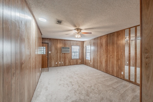 unfurnished room featuring wood walls, a wall mounted AC, light colored carpet, a textured ceiling, and ceiling fan