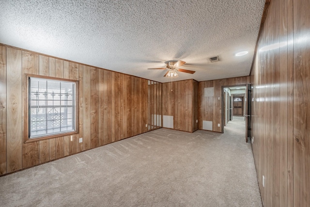 empty room featuring ceiling fan, light colored carpet, a textured ceiling, and wood walls