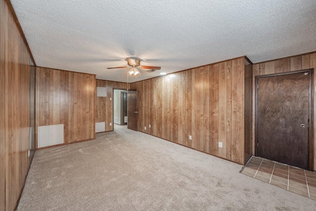 unfurnished bedroom with ceiling fan, light colored carpet, wooden walls, and a textured ceiling