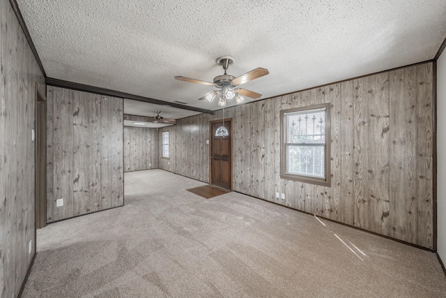 carpeted empty room with ceiling fan, crown molding, wooden walls, and a textured ceiling