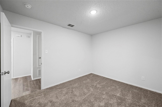 spare room featuring a textured ceiling and dark colored carpet