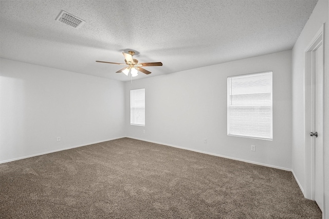 spare room featuring ceiling fan, dark carpet, and a wealth of natural light