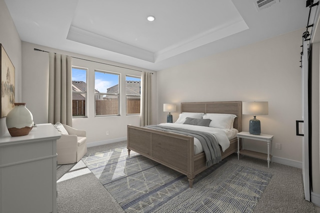 bedroom featuring a barn door, visible vents, light colored carpet, and a tray ceiling