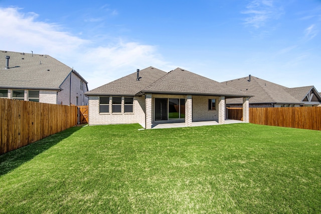 rear view of property with roof with shingles, a fenced backyard, brick siding, a patio area, and a yard
