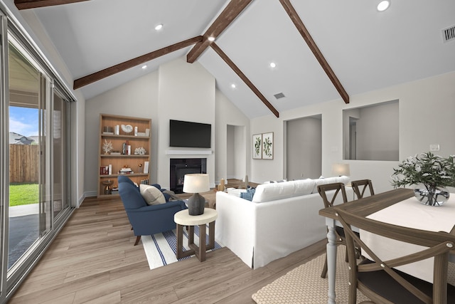 living area featuring light wood-style flooring, beam ceiling, visible vents, a glass covered fireplace, and recessed lighting