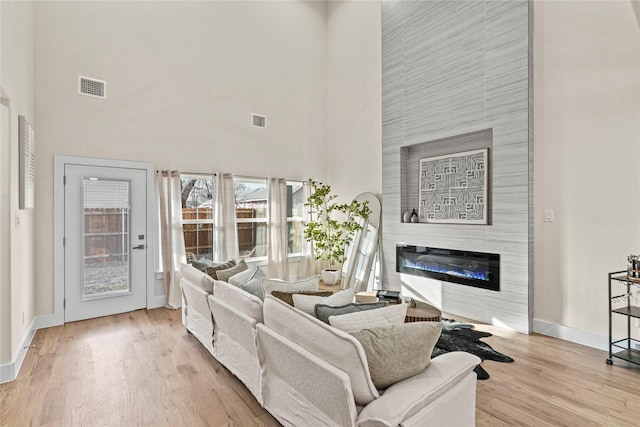 living room featuring a towering ceiling, a large fireplace, and light wood-type flooring