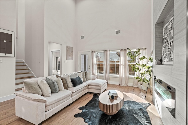 living room with a towering ceiling, a fireplace, and light wood-type flooring