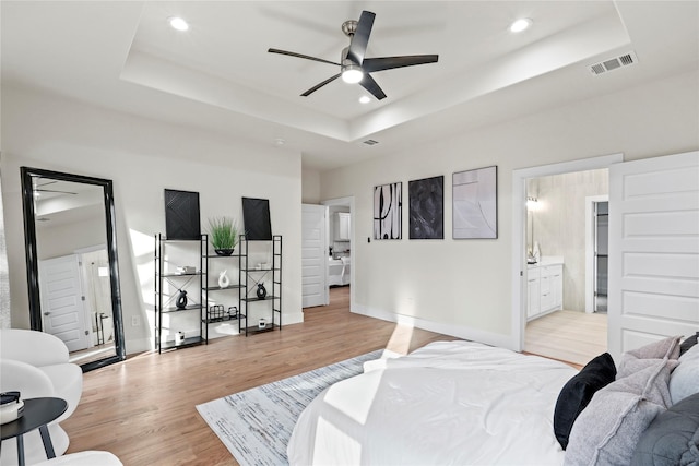 bedroom featuring a tray ceiling, ensuite bathroom, and light wood-type flooring