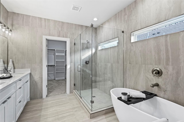 bathroom featuring vanity, plus walk in shower, and tile walls