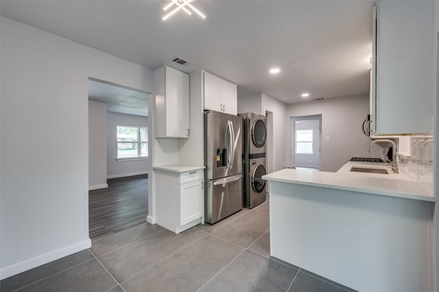 kitchen with stainless steel appliances, stacked washer / drying machine, sink, white cabinetry, and kitchen peninsula