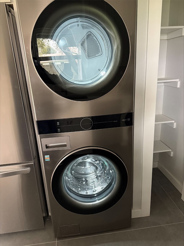 laundry area with stacked washing maching and dryer and dark tile patterned floors